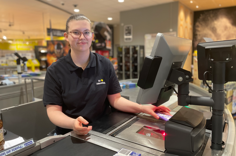 Mitarbeiterin mit einem Lächeln an der Kasse von EDEKA Georg