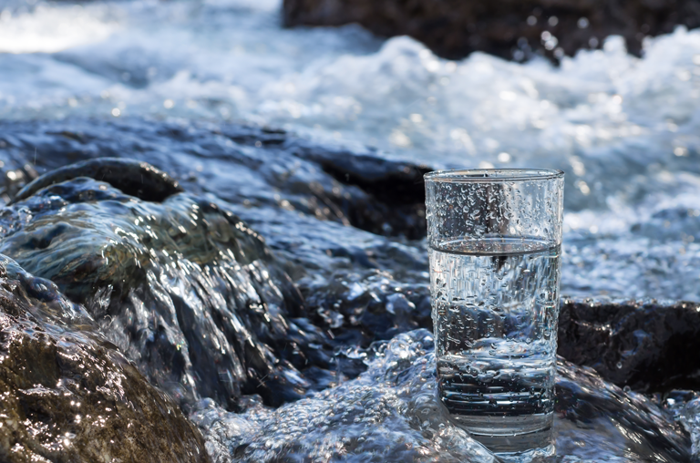 Ein Glas Wasser steht in einem Flusslauf - Imagebild zur Bedeutung und zum Hintergrund frischen Mineralwassers