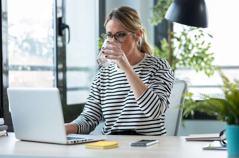 Eine Frau am Schreibtisch trinkt Wasser
